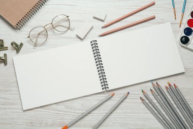 Düz kompozisyon ve beyaz ahşap masa üzerinde boş çizim defteri. Metin için boşluk