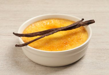 Lezzetli creme brulee ve vanilya çubukları beyaz ahşap masada, yakın çekim görüntüsü