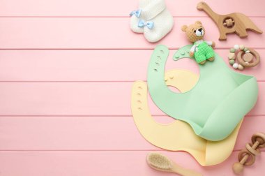 Pembe ahşap arka planda silikon bebek önlükleri, oyuncakları ve aksesuarları olan düz bir kompozisyon. Metin için boşluk