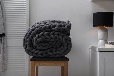 Koyu gri örgü örgü battaniye. Odadaki ahşap tabureye sarılmış.