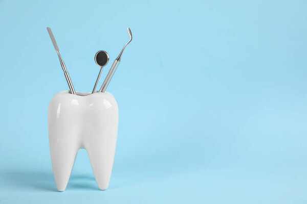 Tooth shaped holder with set of dentist's tools on light blue background. Space for text