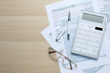 Hesap makinesi, dokümanlar, kalem ve bardaklar ahşap masanın üzerinde, düz yerde yazı için yer var. Vergi muhasebesi
