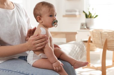 Anne, evdeki küçük bebeğine vücut kremi sürüyor.