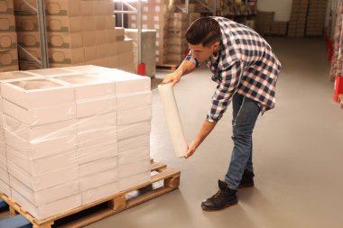 Depoda işçi kutularını streç filme sarıyorlar.