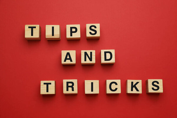 Phrase Tips And Tricks made of wooden cubes with letters on red background, flat lay