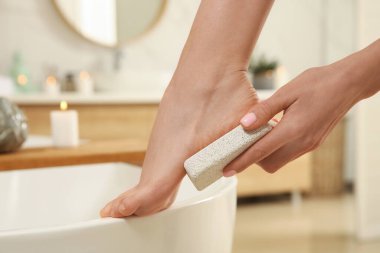 Banyodaki ölü deriyi çıkarmak için sünger taşı kullanan kadın, yakın plan.