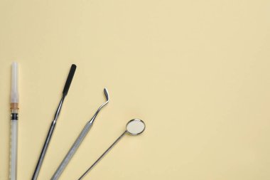 Dişçi aletleri ve şırıngalar soluk sarı arka planda, düz yerde. Metin için boşluk