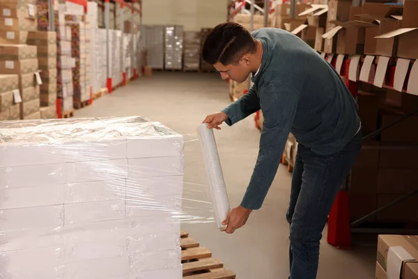 Depoda işçi kutularını streç filme sarıyorlar.