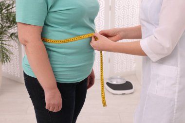 Klinikte kilolu kadının belini bantla ölçen beslenme uzmanı.
