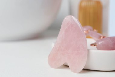 Rose Quartz gua sha aracı ve beyaz masadaki doğal yüz silindiri, yakın plan. Metin için boşluk