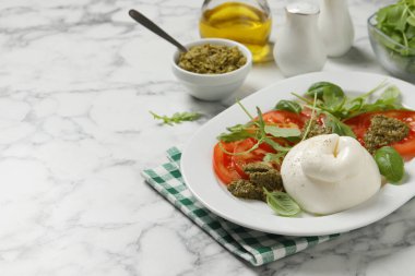 Beyaz mermer masada servis edilen domates, roka ve pesto soslu nefis burata salatası. Metin için boşluk