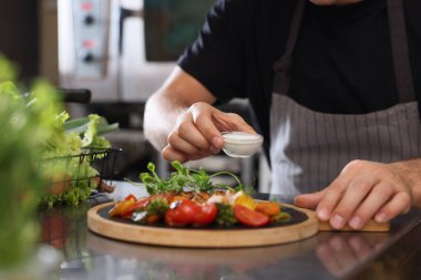 Profesyonel aşçı, restoranın mutfağında pişirilen lezzetli yemeklere bir kase sos koyar.