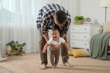 Babası, kızına evde yürümeyi öğrenirken bakıyor.