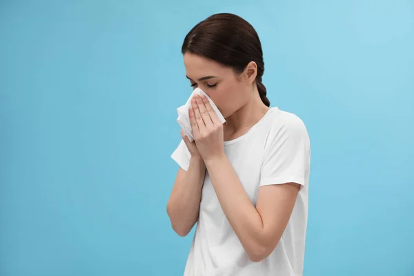 ライトブルーの背景に鼻を吹いている女性 風邪の症状 — ストック写真