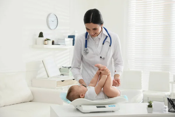 年轻儿科医生在诊所称可爱的小宝宝的重量 — 图库照片