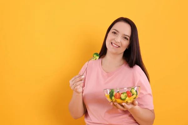 黄色の背景にサラダを食べる美しい太りすぎの女性 テキストのためのスペース 健康的な食事 — ストック写真