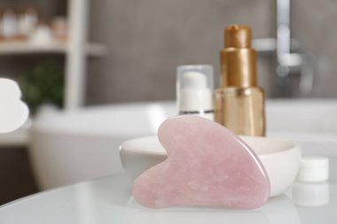 Rose Quartz gua sha aracı ve kozmetik ürünleri banyodaki beyaz masanın üzerinde. Metin için boşluk