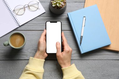 Gri ahşap masada akıllı telefonlu bir kadın.