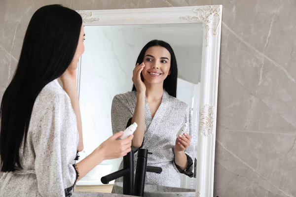 Vacker Ung Kvinna Som Tillämpar Återfuktande Kräm Nära Spegel Badrummet — Stockfoto