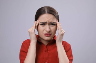 Açık gri arka planda baş ağrısı çeken bir kadın. Soğuk belirtileri