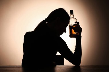 Alkol bağımlılığı. Ahşap masada elinde viski şişesi olan bir kadın silueti.
