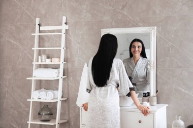 Güzel genç bir kadın banyo aynasında kendine bakıyor.