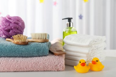 Beyaz masadaki havlular, plastik ördekler ve bebek bakım ürünleri.