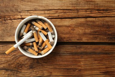 Ahşap masada sigara izmaritleriyle dolu seramik kül tablası, üst manzara. Metin için boşluk