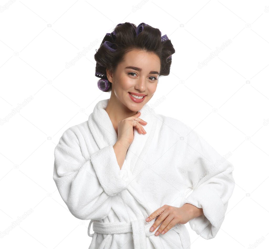 Happy young woman in bathrobe with hair curlers on white background