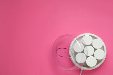 Pembe arka planda kavanozları olan modern yoğurt imalatçısı. Metin için boşluk