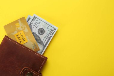 Dolar banknotları ve cüzdanda kredi kartı sarı arka planda, üst manzarada mesaj için yer var. Nakit para kavramı