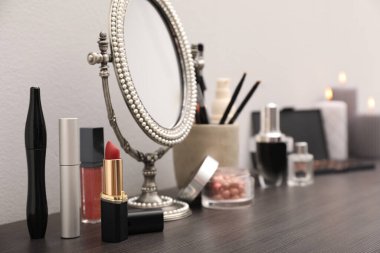 Ayna, mumlar ve farklı makyaj ürünleri. Duvarın yanındaki koyu ahşap makyaj masasında.