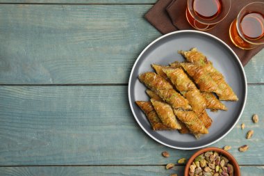 Fıstıklı enfes baklavalar, dağınık fındıklar ve açık mavi ahşap masada sıcak çay. Metin için boşluk