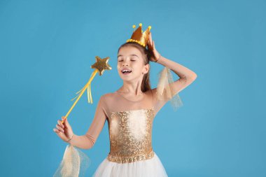 Peri elbiseli, altın tacı ve açık mavi arka planda sihirli değneği olan tatlı bir kız. Küçük prenses.