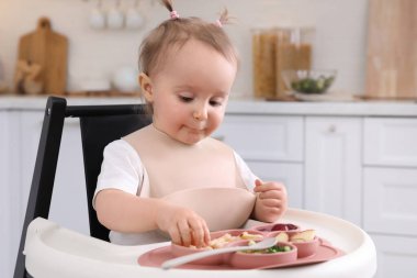 Sevimli küçük bebek mutfakta yüksek sandalyede yemek yiyor.