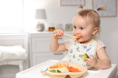 Evdeki yüksek sandalyede yemek yiyen şirin bir bebek.