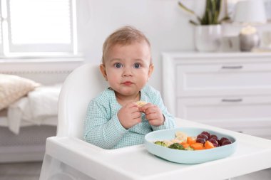 Evdeki yüksek sandalyede yemek yiyen şirin bir bebek.