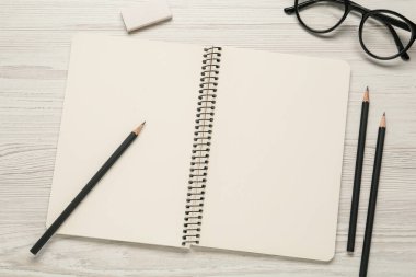 Düz kompozisyon ve beyaz ahşap masa üzerinde boş çizim defteri. Metin için boşluk