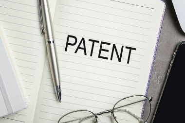 Kelime PATENT ile defter, gri masa üzerinde kalem ve gözlük, üst görünüm