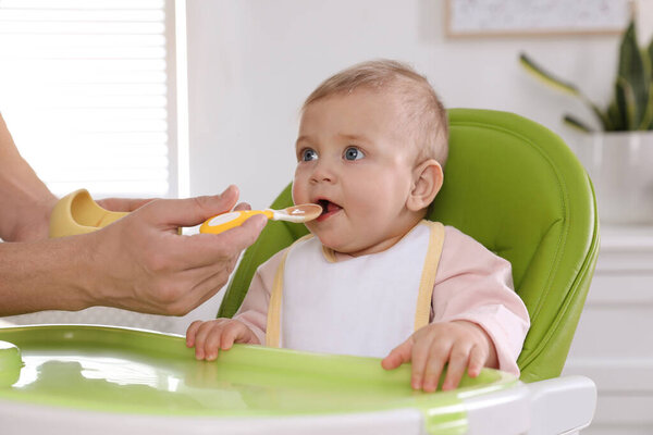 Father feeding his cute little baby healthy food at home