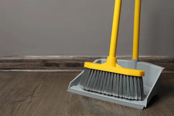 stock image Plastic broom with dustpan near grey wall indoors. space for text