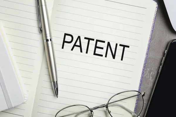 Patent 字样的笔记本 灰色桌子上有钢笔和眼镜 顶部视图 — 图库照片