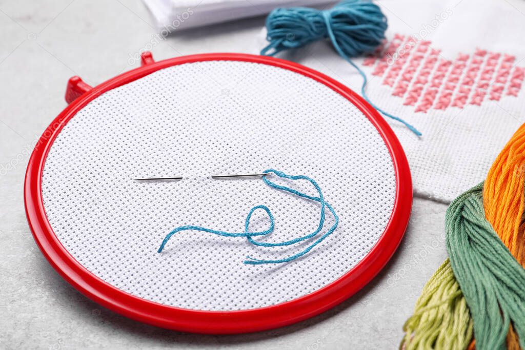 Embroidery hoop with fabric and needle on white table, closeup