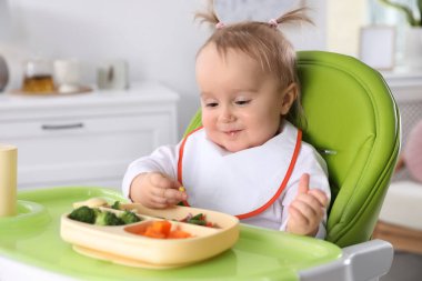 Evdeki yüksek sandalyede yemek yiyen şirin bir bebek.