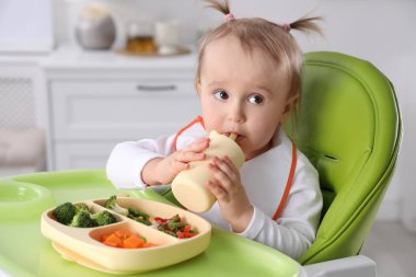 Şirin küçük bebek, yüksek sandalyedeki şişeden içiyor.
