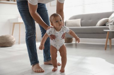 Babası, kızına evde yürümeyi öğrenirken bakıyor.
