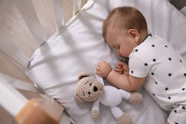 可爱的小宝宝 带着奶嘴和玩具睡在室内的婴儿床里 — 图库照片