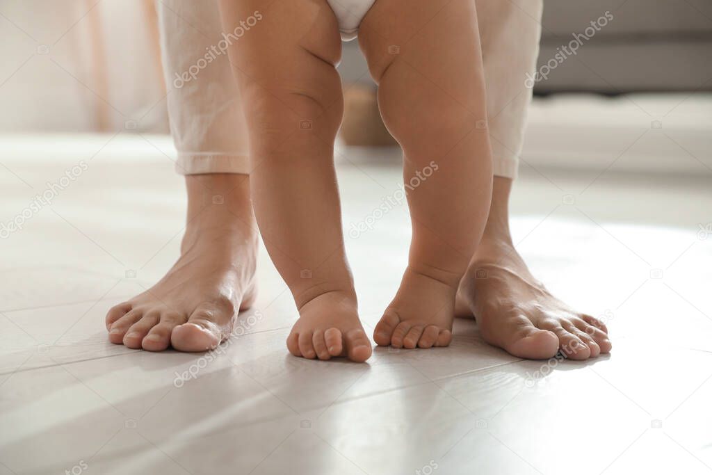 Mother supporting her baby daughter while she learning to walk at home, closeup