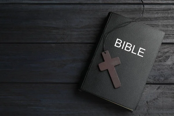 基督教十字架和圣经在黑色木制桌子上 顶部视图 案文的篇幅 — 图库照片
