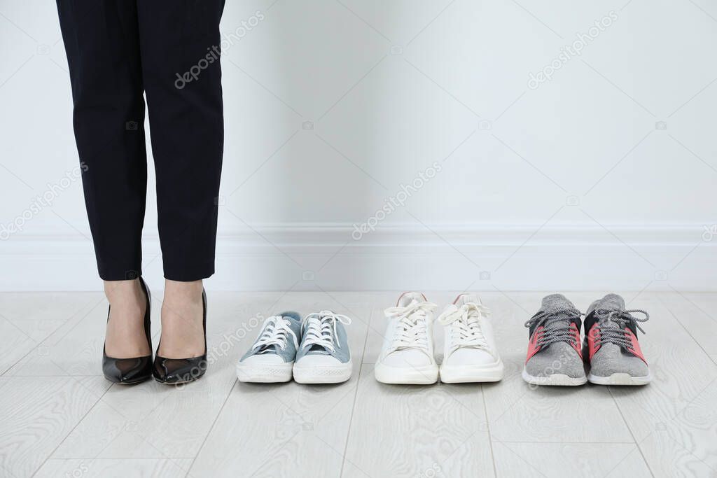 Different comfortable sneakers near businesswoman wearing high heel shoes indoors, closeup
